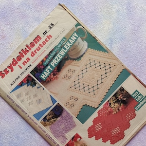 Peut inclure: Magazine polonais "Szydełkiem i na drutach" présentant des patrons de crochet et de broderie. La couverture affiche divers motifs de crochet et de broderie en blanc, rouge et bleu. Le magazine est sur une surface texturée, violet clair. Mesures non applicables.
