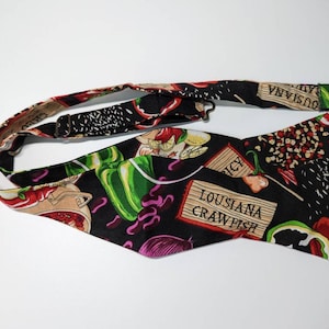 May include: A black bow tie with a colourful print of peppers, spices, and the text "Louisiana Crawfish".