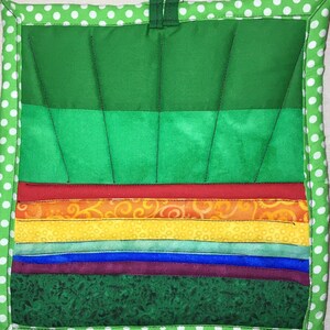 May include: A green, red, orange, yellow, blue and purple quilted pot holder with a white polka dot border. The pot holder has a loop for hanging.