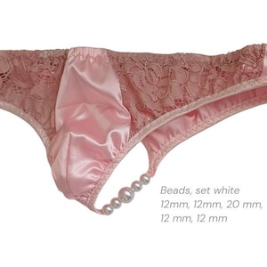 Könnte beinhalten: Rosa Satin- und Spitzenunterwäsche mit String-Rückseite. Die Vorderseite ist aus Satin, die Seiten aus Spitze. Eine Kette weißer Perlen verziert den String. Der Text "Beads, set white" und die Maße sind sichtbar.