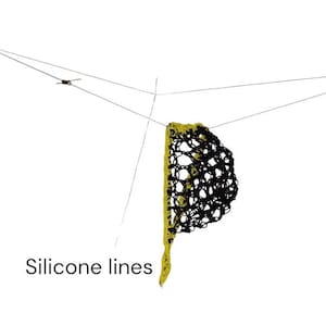 Puede incluir: Una red negra con un borde amarillo está suspendida por finas líneas de silicona grises sobre un fondo blanco. El texto "Silicone lines" es visible cerca de las líneas.
