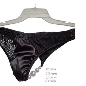 May include: Black satin underwear with lace detailing and a pearl accent. The underwear is displayed on a white hanger against a white background. The pearl accent is made up of 4 pearls, with sizes ranging from 1.2 cm to 2.8 cm.