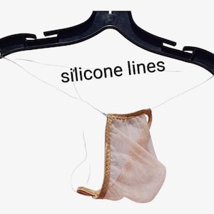 以下が含まれることがあります： 黒いプラスチック製のハンガーに、シリコンラインで吊るされたシアーなヌードカラーの衣服。衣服には金のトリムが付いています。「silicone lines」の文字が画像に印刷されています。