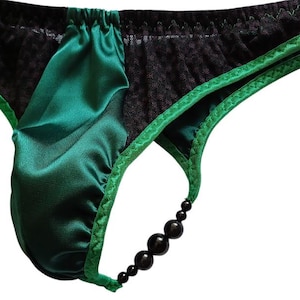 May include: A pair of underwear featuring a combination of emerald green satin fabric and black textured mesh panels. The garment is accented with green trim and a side strap detail consisting of four graduated black beads connected to the waistband.