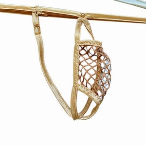 Könnte beinhalten: Ein goldfarbener Tanga mit metallischem Glanz und einer zentralen Tasche aus braunem, grobmaschigem Netzstoff. Das Kleidungsstück verfügt über dünne, verstellbare elastische Riemen und einen Rahmen, der den Netzstoff in Form hält.