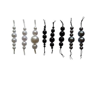 May include: A collection of beaded strands in different colours and sizes. The strands feature white, black, and grey beads, varying from small to large, with a glossy finish. Each strand is strung on a thin cord, creating a decorative element.