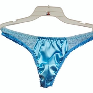 May include: Light blue satin thong underwear with lace detailing on the waistband and edges. The underwear is hanging on a white plastic hanger.