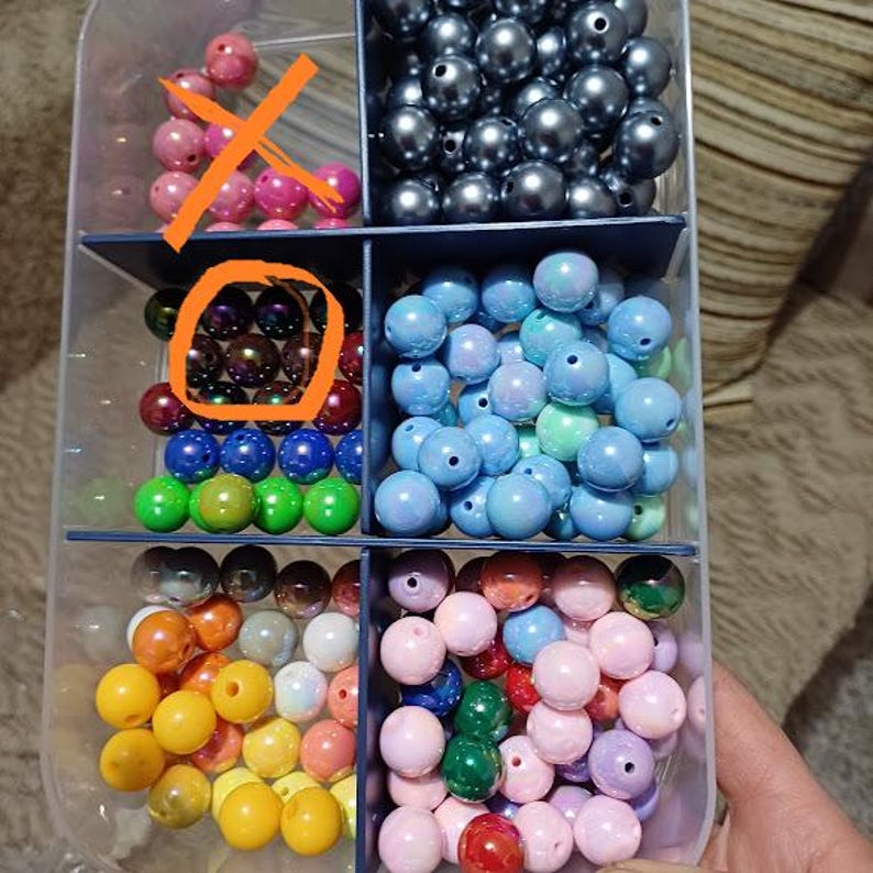 May include: A clear plastic organiser filled with various colourful beads. The beads are in shades of pink, silver, blue, green, yellow, and red. The beads are round and have a hole through the centre, perfect for jewellery making.