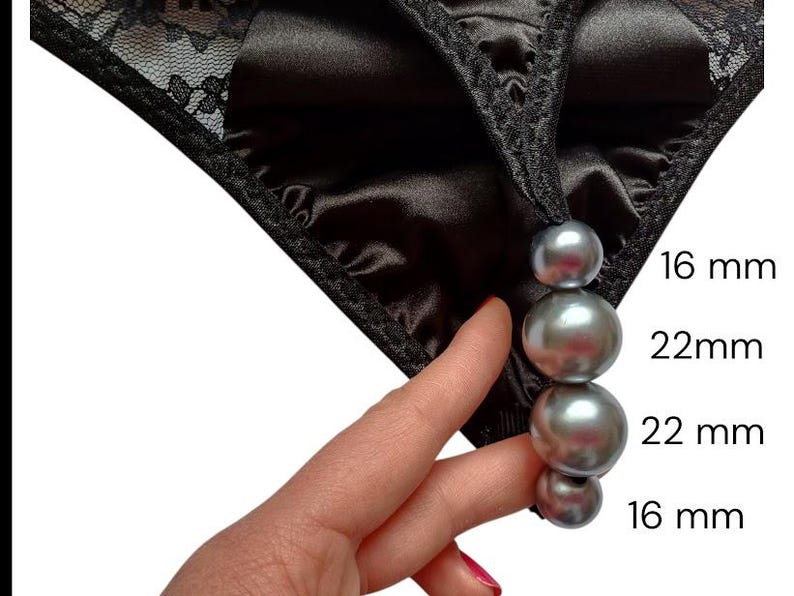 May include: Black satin underwear with lace detailing. A string of four grey beads, measuring 1.6 cm and 2.2 cm, hangs from the garment. The image shows a close-up of the underwear and beads.