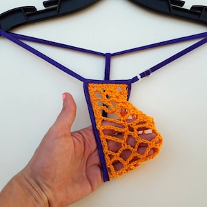 May include: Orange crocheted lingerie with purple straps. The lingerie is hanging on a black hanger.