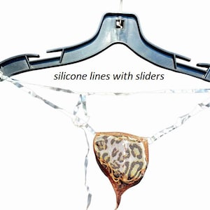Puede incluir: Un tanga con diseño de estampado de leopardo, colgado de una percha de plástico negro. El tanga tiene una combinación de colores marrón y beige, con el texto "silicone lines with sliders" encima.