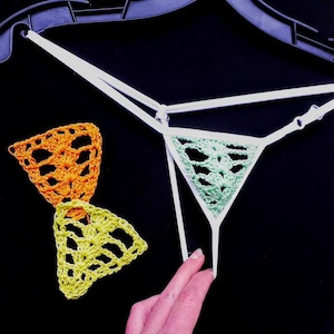 May include: A white crocheted bikini bottom with a green and orange crocheted bow tie.