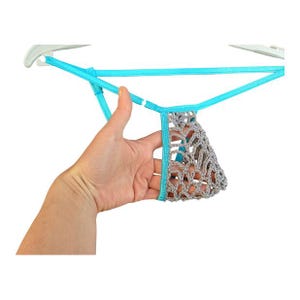 Peut inclure: Un string en crochet gris et turquoise. Le string est maintenu par une ficelle turquoise et un cintre blanc. La partie en crochet est de couleur gris clair.