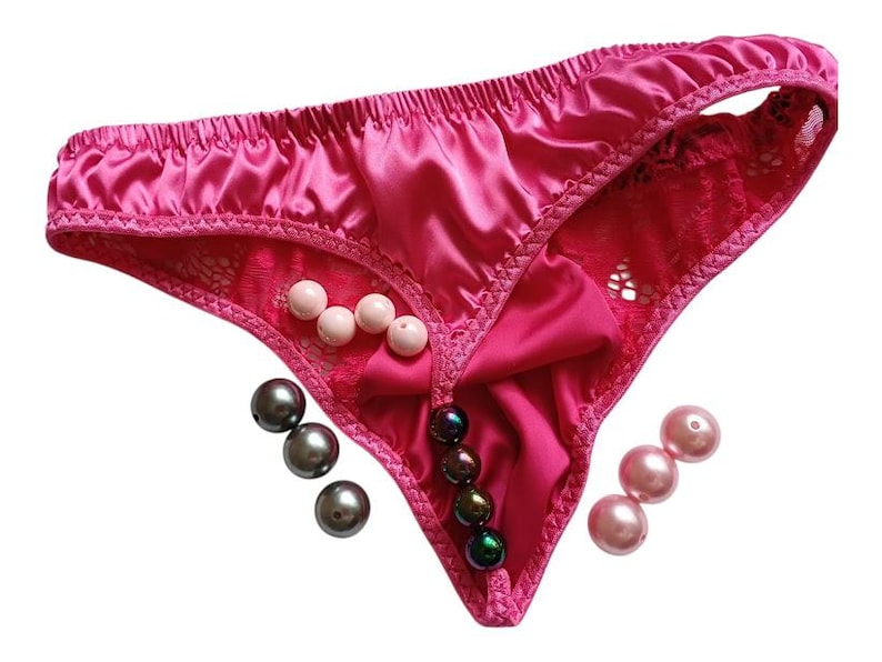 May include: Bright pink satin thong underwear with lace inserts and a bow. The underwear is decorated with pearl beads in white, grey, and pink. The garment is designed with a thong style.