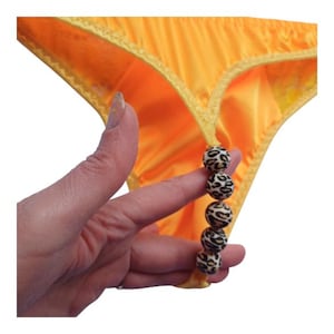Op de afbeelding: Felgeel string-slipje met een decoratieve ketting van kralen met luipaardprint. Het ondergoed heeft een satijnachtige glans en een delicate, geschulpte rand.