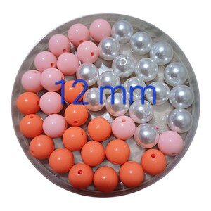 May include: A selection of 12mm round beads in shades of light pink, orange, and pearlescent white. The beads are displayed in a circular arrangement, ideal for crafting or jewellery projects.
