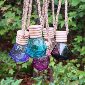 May include: Five diamond-shaped glass bottles with wooden tops and twine strings. The bottles are filled with different colored liquids: blue, teal, purple, pink, and black.