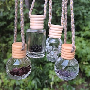 May include: Four glass car air fresheners with different shapes and colors of crystals inside. The fresheners are hanging from beige and gold cords.