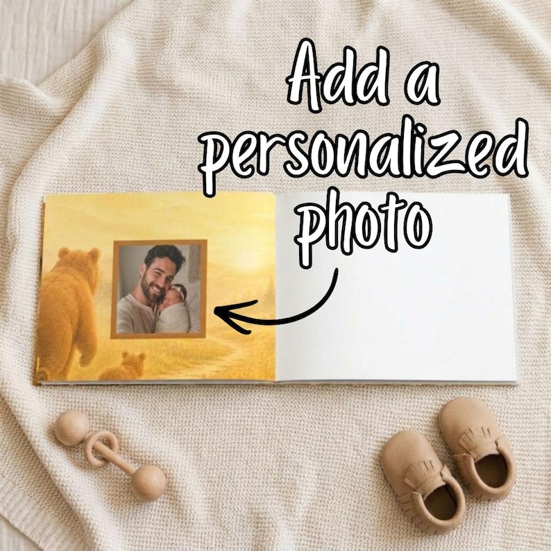 May include: An open baby photo album with a picture of a father and child, a wooden rattle, and a pair of tan baby shoes. The album has the text "Add a personalized photo". The left page has a bear illustration.