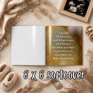 May include: An open softcover book with the text "To my daddy, this book is for you..." on a gold-toned page. The book is 8 x 8 inches. The image also shows baby shoes, a framed sonogram, and a wooden toy.