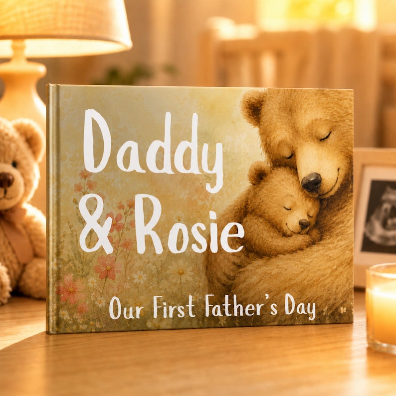 May include: A personalized book titled "Daddy & Rosie" with a heartwarming illustration of two bears embracing. The cover features the text "Our First Father's Day" and is set on a wooden surface, with a teddy bear and lamp in the background.