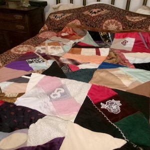 May include: A patchwork quilt constructed from various fabric scraps in diverse colors including pink, black, white, purple, and green. The quilt features irregular geometric shapes, some with embroidered floral and lace details, stitched together with visible seams and decorative trim.