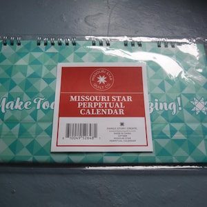 May include: A spiral-bound perpetual calendar with a geometric teal and white design. The calendar features a red label with the text "MISSOURI STAR PERPETUAL CALENDAR". The words "Make Today" and "Bing!" are also visible.
