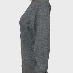 以下が含まれることがあります： グレーの長袖セーター、ハイネック、ジッパー付き。セーターはウエストにリブ編みのディテールがあり、ぴったりとしたフィット感です。生地は柔らかいニットのようです。袖は長く、手首で終わります。