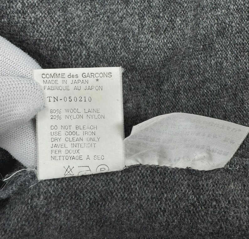 以下が含まれることがあります： 黒い持ち手と「But First, Coffee」のテキストが黒い太字で書かれた白いセラミックマグ。マグカップはぼやけた背景に置かれており、居心地の良い環境を示唆しています。