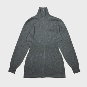 以下が含まれることがあります： ハイネックのグレーのジップアップセーター。セーターはウエストがフィットし、長袖です。ジッパーはセーターの全長にわたって走っています。素材は柔らかいニットのようです。