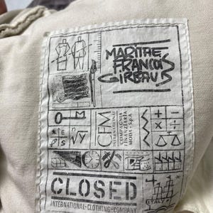 May include: A white ceramic mug with a black handle and the text "But First, Coffee" in a bold, black font. The mug is set against a blurred background, suggesting a cosy setting.