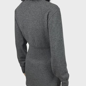 以下が含まれることがあります： リブ編みのウエストディテールと長袖が特徴のグレーのセーター。セーターはクルーネックで、フィットしたシルエットです。生地は柔らかいニットのようです。モデルは黒いパンツを着用しています。