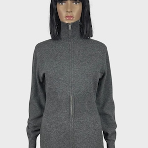 以下が含まれることがあります： ハイネックのグレーのジップアップセーター。セーターはリブ編みのウエストディテールとフルレングスのジッパーが付いています。袖は長く、生地は柔らかいニットのようです。マネキンに着せられています。