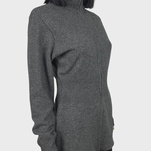 以下が含まれることがあります： グレーの長袖セーター。ハイネックのリブ編みカラーとフルレングスのジッパーが付いています。セーターはリブ編みのウエストディテールがあり、柔らかいニット素材で作られています。マネキンに着せられています。