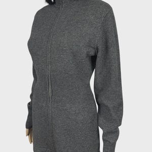 以下が含まれることがあります： ハイネックのグレーのジップアップセーター。セーターはリブ編みのウエストと袖口、シルバーのジッパーが付いています。長袖セーターはマネキンに展示されています。