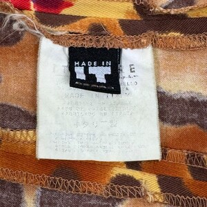 May include: A white tag with black text that reads "MADE IN ITALY" attached to a brown and yellow patterned fabric.