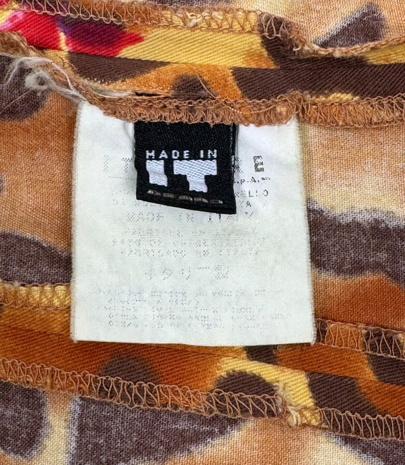 May include: A white tag with black text that reads "MADE IN ITALY" attached to a brown and yellow patterned fabric.