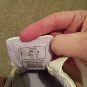 Puede incluir: Primer plano del interior de una zapatilla blanca con forro morado. La etiqueta dice "Leomil FZ012270" e incluye informaci&oacute;n de tallas y el texto "Made in China, Hecho en China, Fabriqu&eacute; en Chine".