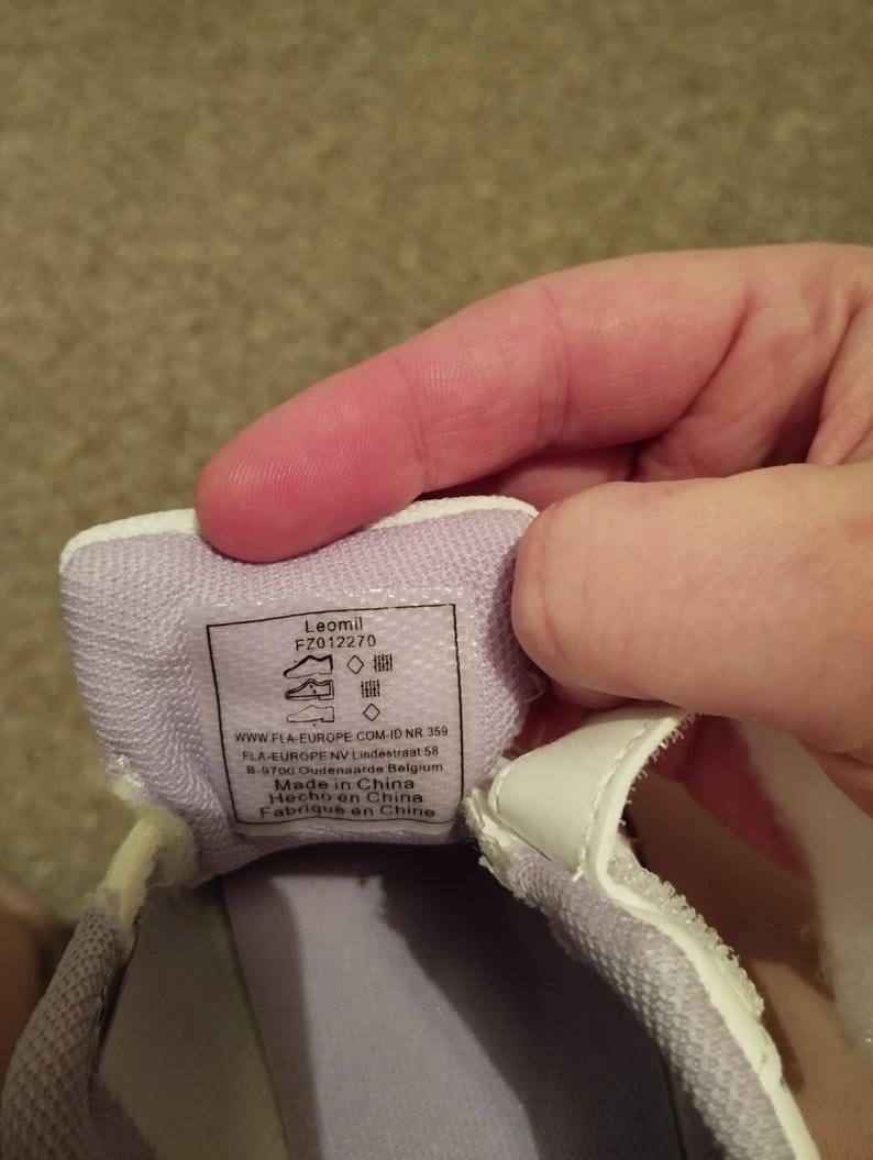 Puede incluir: Primer plano del interior de una zapatilla blanca con forro morado. La etiqueta dice "Leomil FZ012270" e incluye informaci&oacute;n de tallas y el texto "Made in China, Hecho en China, Fabriqu&eacute; en Chine".