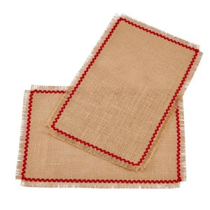 May include: Two brown burlap placemats with red fringe trim. The placemats are stacked on top of each other.