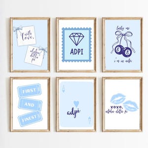 May include: A set of six framed wall art prints featuring light blue backgrounds and dark blue graphics. Designs include notes with bows, a diamond, billiard balls with the text lucky me i'm in adpi, tickets with text, a playing card, and lips.