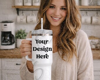 Puede incluir: Vaso blanco con asa y pajita, con el texto "Your Design Here" en negro. El vaso tiene una tapa plateada y un cuerpo blanco. El fondo muestra una cocina con estantes y una cafetera.
