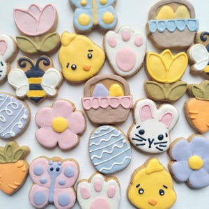 May include: Assortment of decorated sugar cookies in various shapes and colors, including a butterfly, a bunny, a flower, a chick, a basket, a paw print, and a tulip. The cookies are decorated with icing and sprinkles.