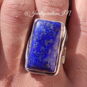 May include: A silver ring with a large rectangular blue lapis lazuli gemstone. The ring is set in a simple silver band.