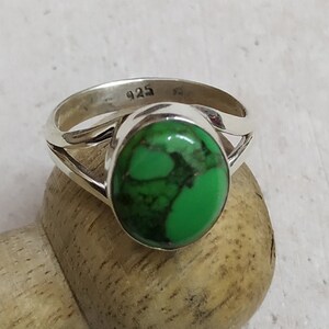 Pode incluir: Um anel de prata com uma pedra oval verde. O anel é marcado com "925" na banda.