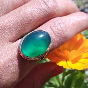 May include: A silver ring with a large oval green gemstone. The ring is on a person's finger.