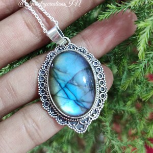Puede incluir: Un collar de cadena de plata con un colgante de plata que presenta una gran piedra de labradorita azul de forma ovalada. El colgante tiene un diseño adornado detallado.