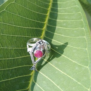 May include: A silver ring with a pink gemstone set in a fish design.