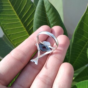 May include: A silver ring with a detailed design featuring a bird with a purple gemstone in its beak.