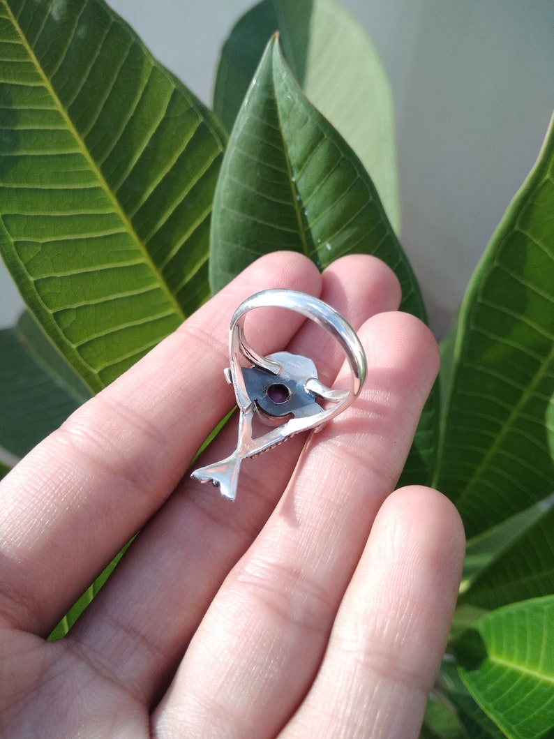 May include: A silver ring with a detailed design featuring a bird with a purple gemstone in its beak.